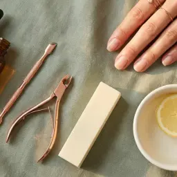 Set per manicure con olio per cuticole unghie, spingicuticole, tronchesino, lima e una fetta di limone in una ciotola.