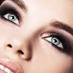 Occhi azzurri intensi con un trucco smokey eyes audace e labbra lucide.