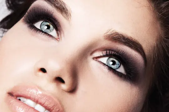 Occhi azzurri intensi con un trucco smokey eyes audace e labbra lucide.
